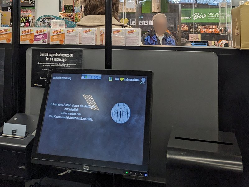 [i]„Es ist eine Aktion durch die Aufsicht erforderlich. Bitte warten Sie. Die Kassenaufsicht kommt zu Hilfe.“[/i] – Edeka in Haar (2025). Wenn man Wein oder andere „Ab-18-Sachen“ kauft, sollte man sich also weiterhin in die Schlange an der Bedienkasse einreihen, da die Selbstscanner-Kassen hier keinen Zeitvorteil darstellen, wenn man erst mal minutenlang warten muss, bis die „Kassenaufsicht“ kommt und den Bezahlvorgang „freischaltet“...